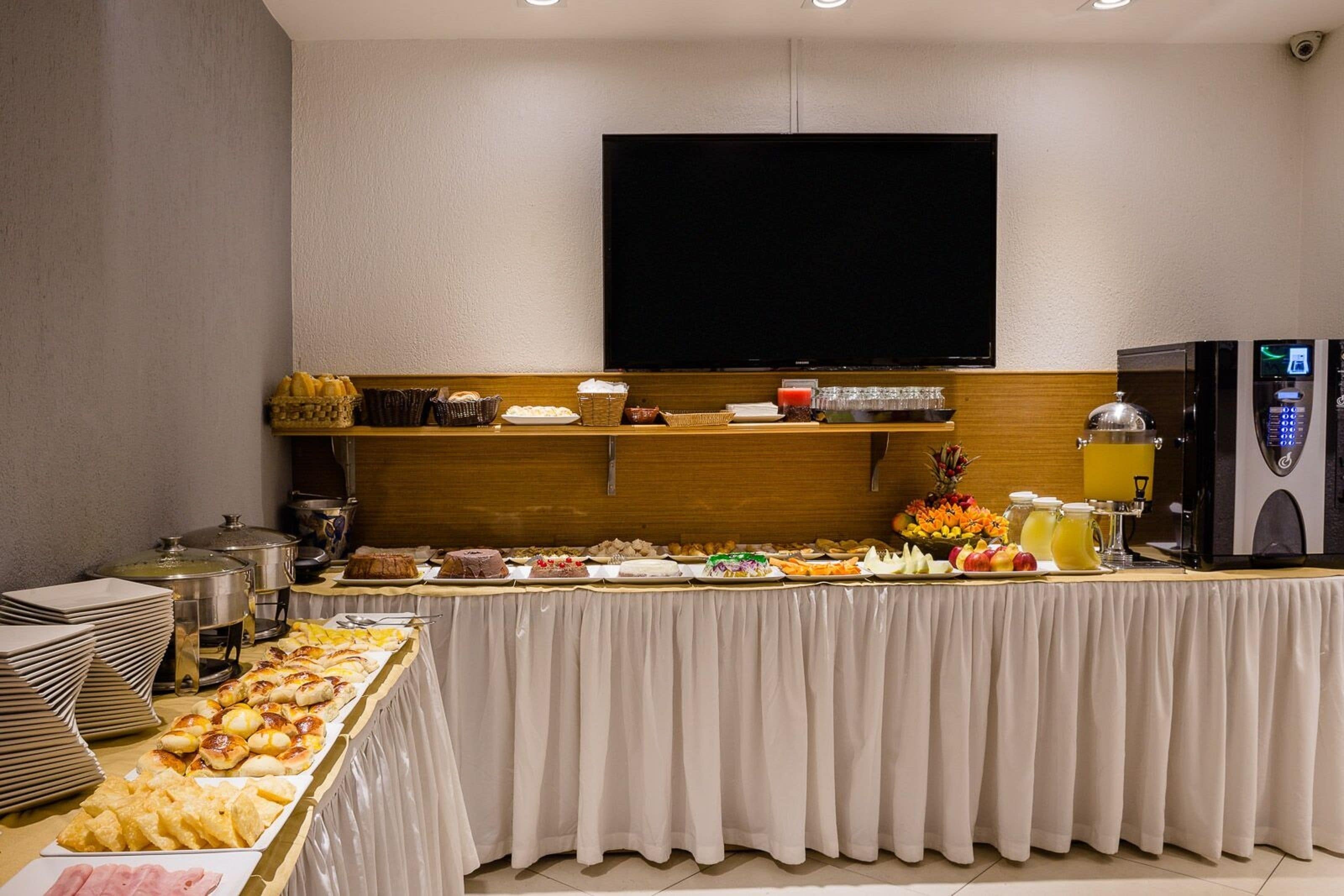 A buffet setup with various food items, a television above, and a refrigerator to the right.