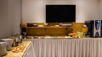 A buffet setup with various food items, a television above, and a refrigerator to the right.