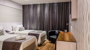 A hotel room with two beds, a desk, a chair, and a large window with curtains.