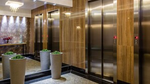 A modern elevator area with wood paneling and stainless steel doors, accompanied by cylindrical planters with greenery.