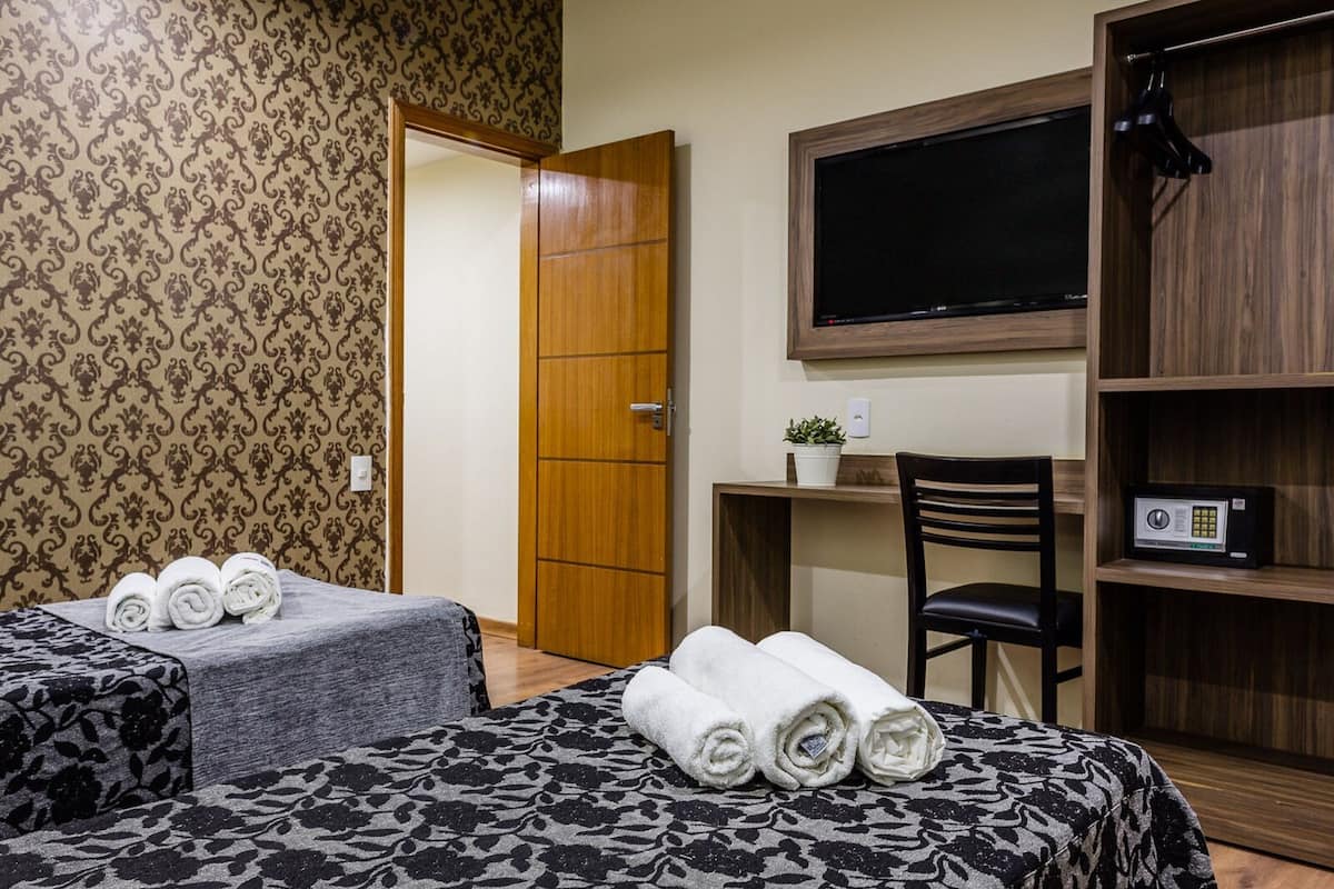 Una habitación de hotel con dos camas, un escritorio con una silla, un televisor y una estantería.