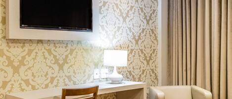 A hotel room with a bed, a desk with a chair, a television, and a lamp.