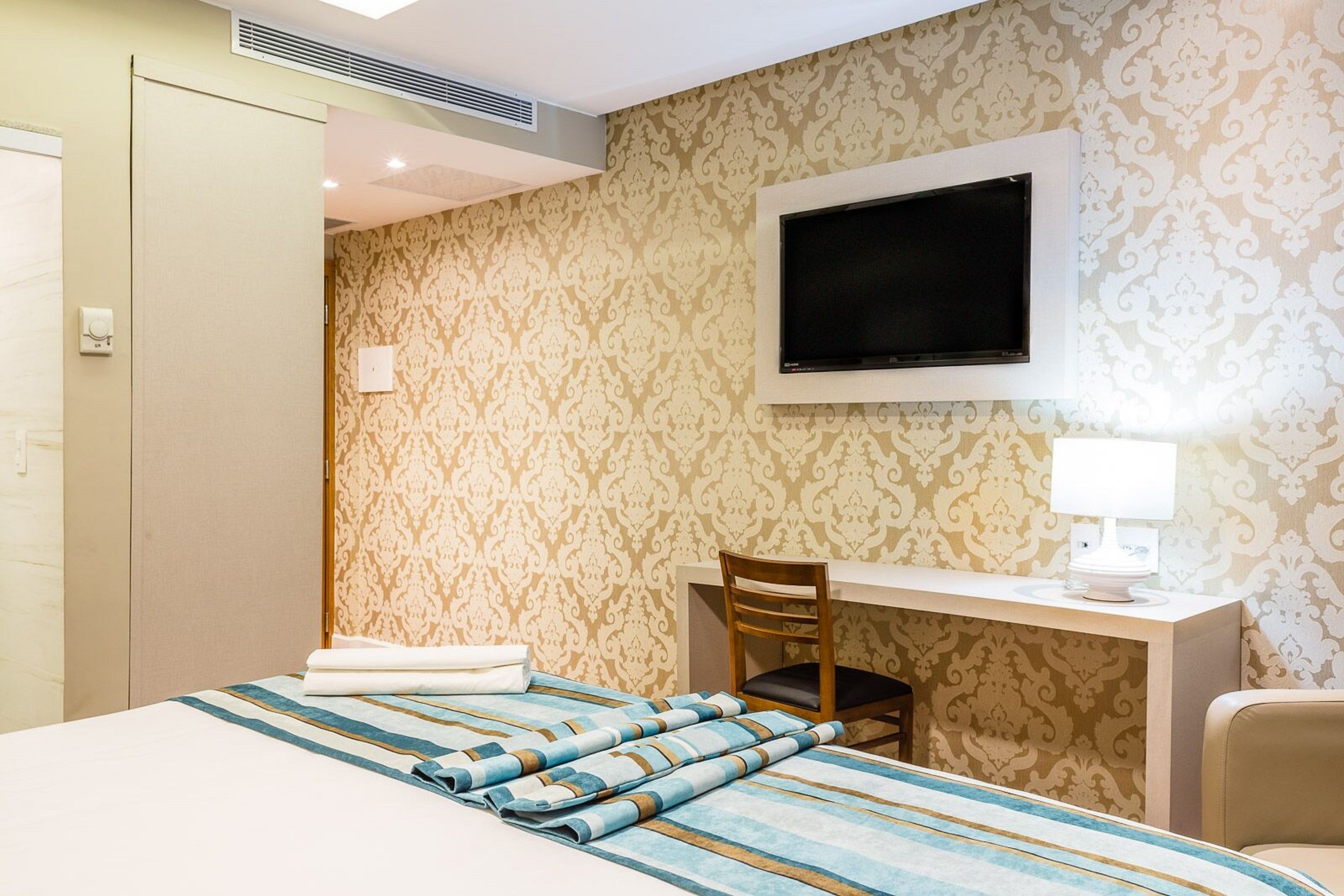 Una habitación de hotel con cama, escritorio, silla, televisor y lámpara.
