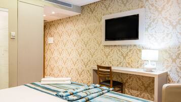 A hotel room with a bed, a desk, a chair, a TV, and a lamp.