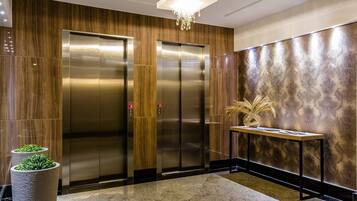 Un área de ascensores moderna con dos ascensores, suelo de mármol y un panel decorativo en la pared.