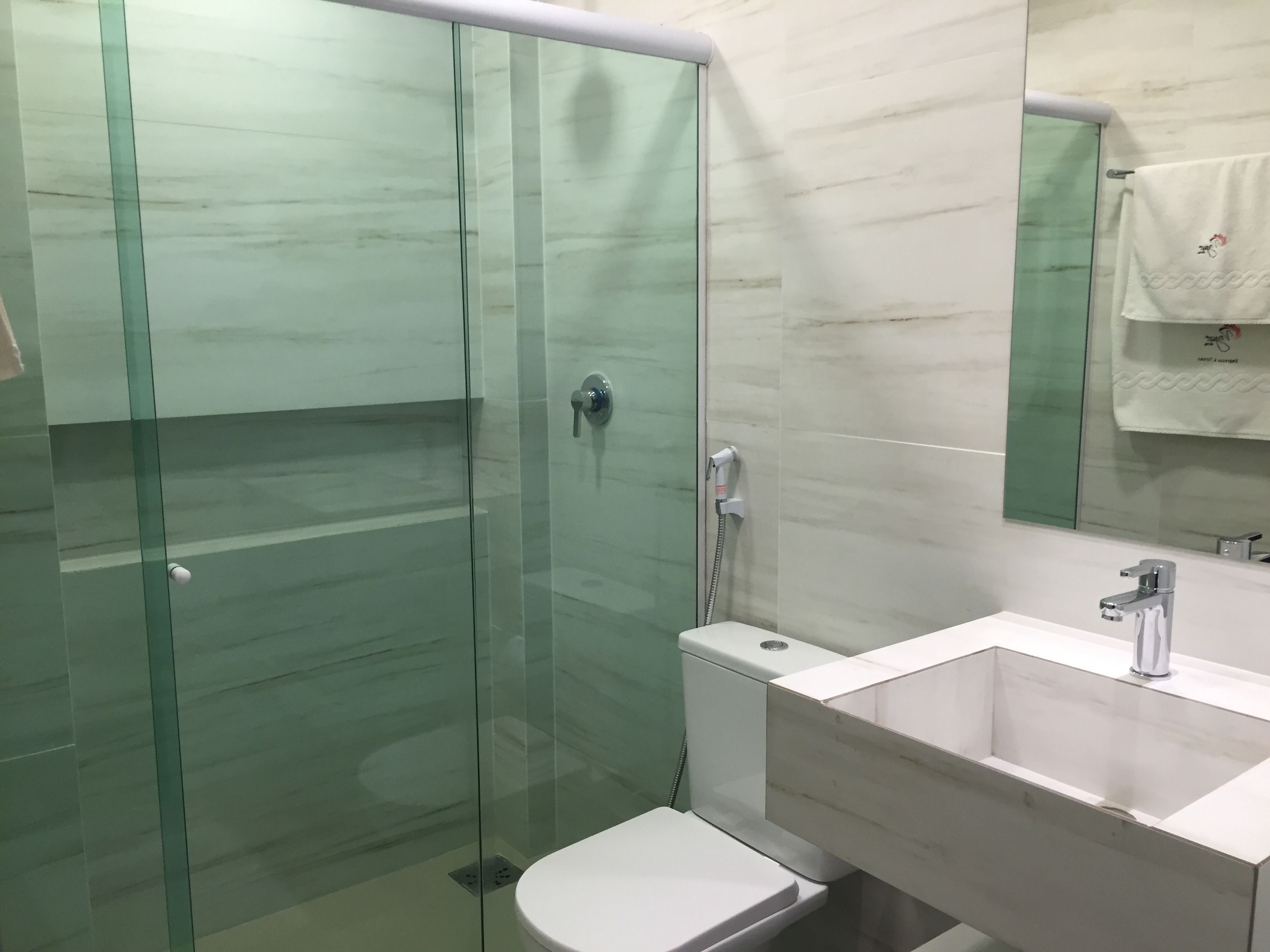 Un baño moderno con ducha acristalada, inodoro blanco y lavamanos con espejo.