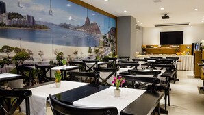 A restaurant with tables set for dining, a large mural of a cityscape on the wall, and a kitchen area in the background.