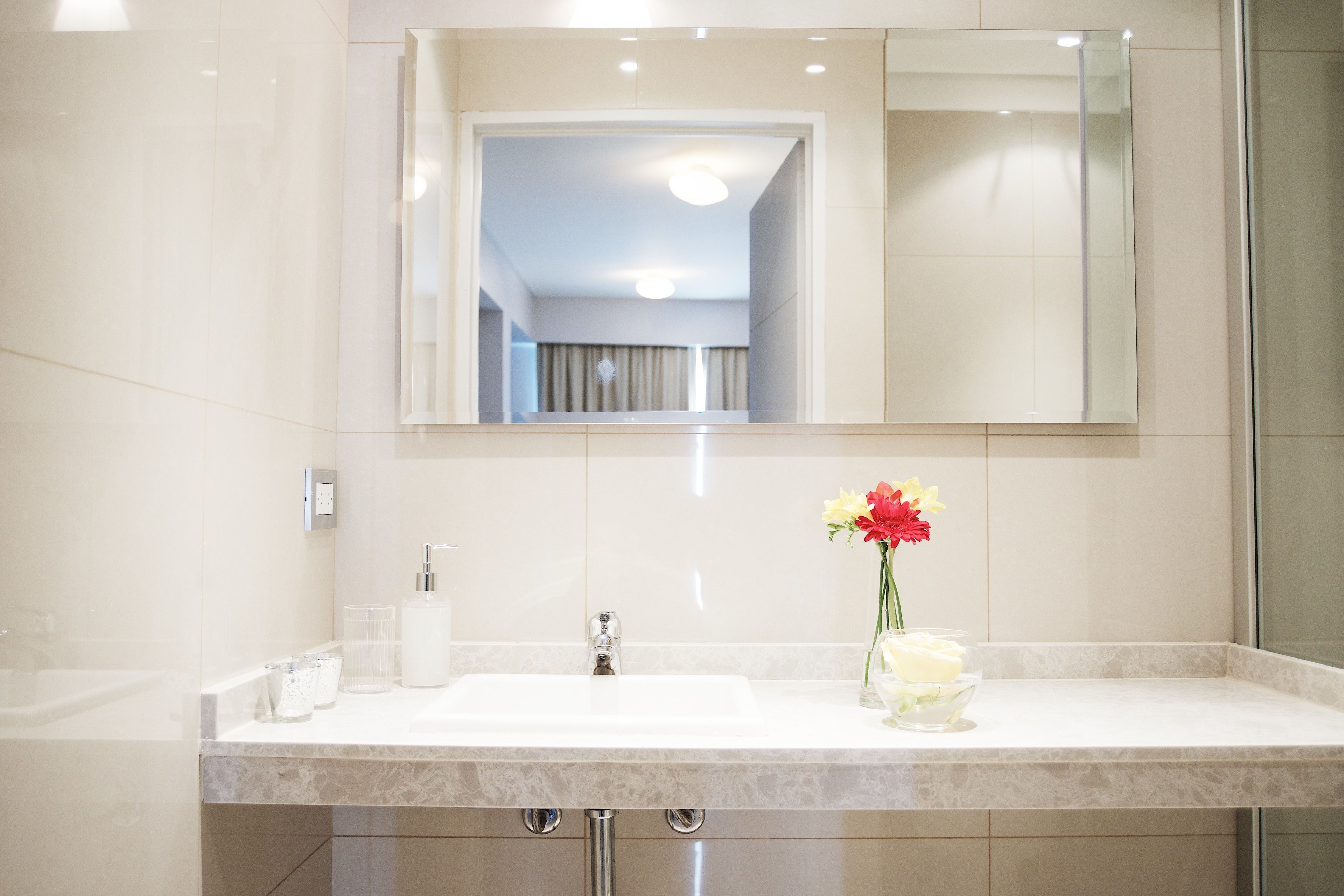 Un baño moderno con un espejo grande, un lavamanos y un jarrón con flores.