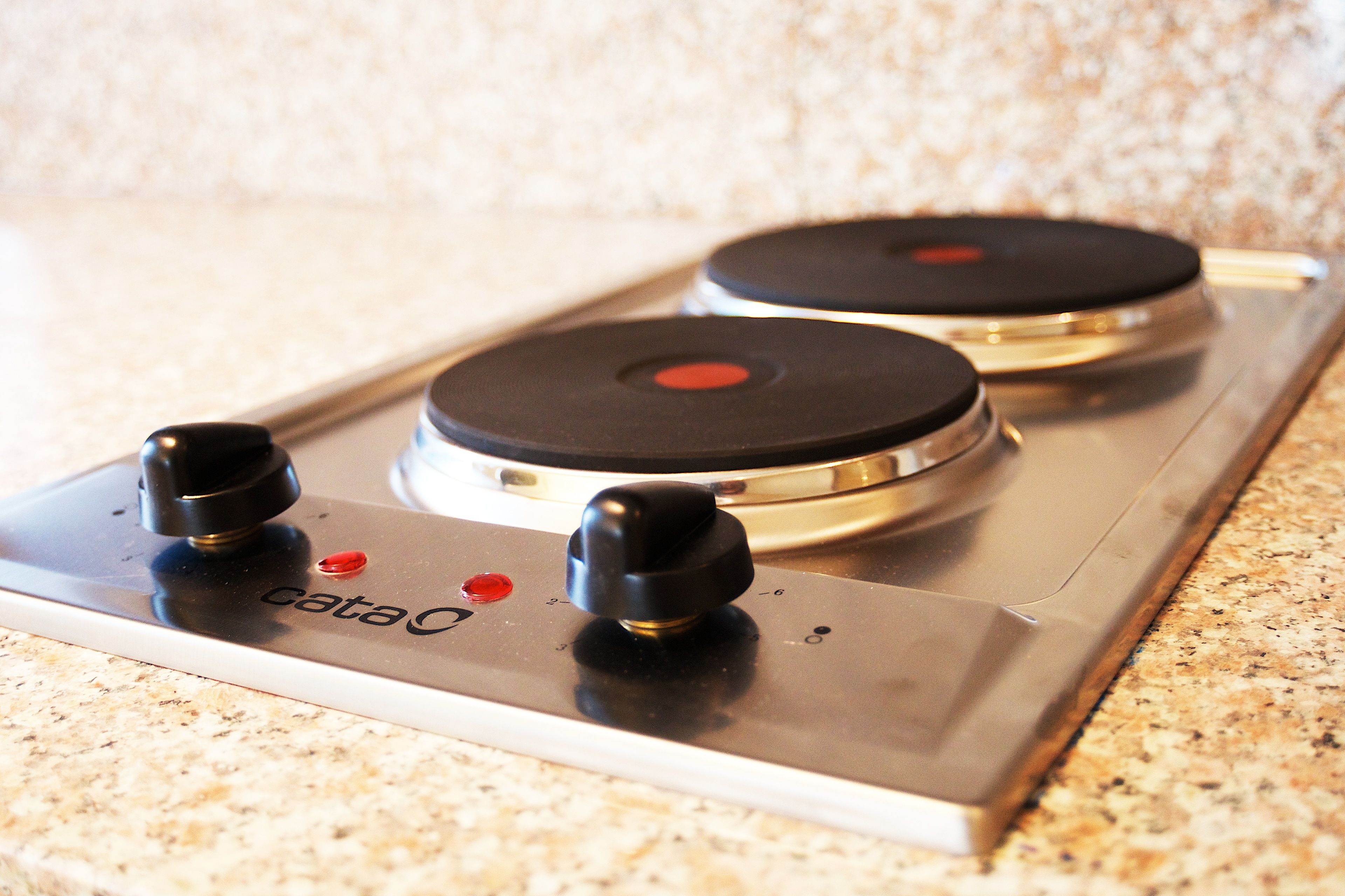 A kitchen with a stainless steel stove top featuring three burners and a control panel with a red button.