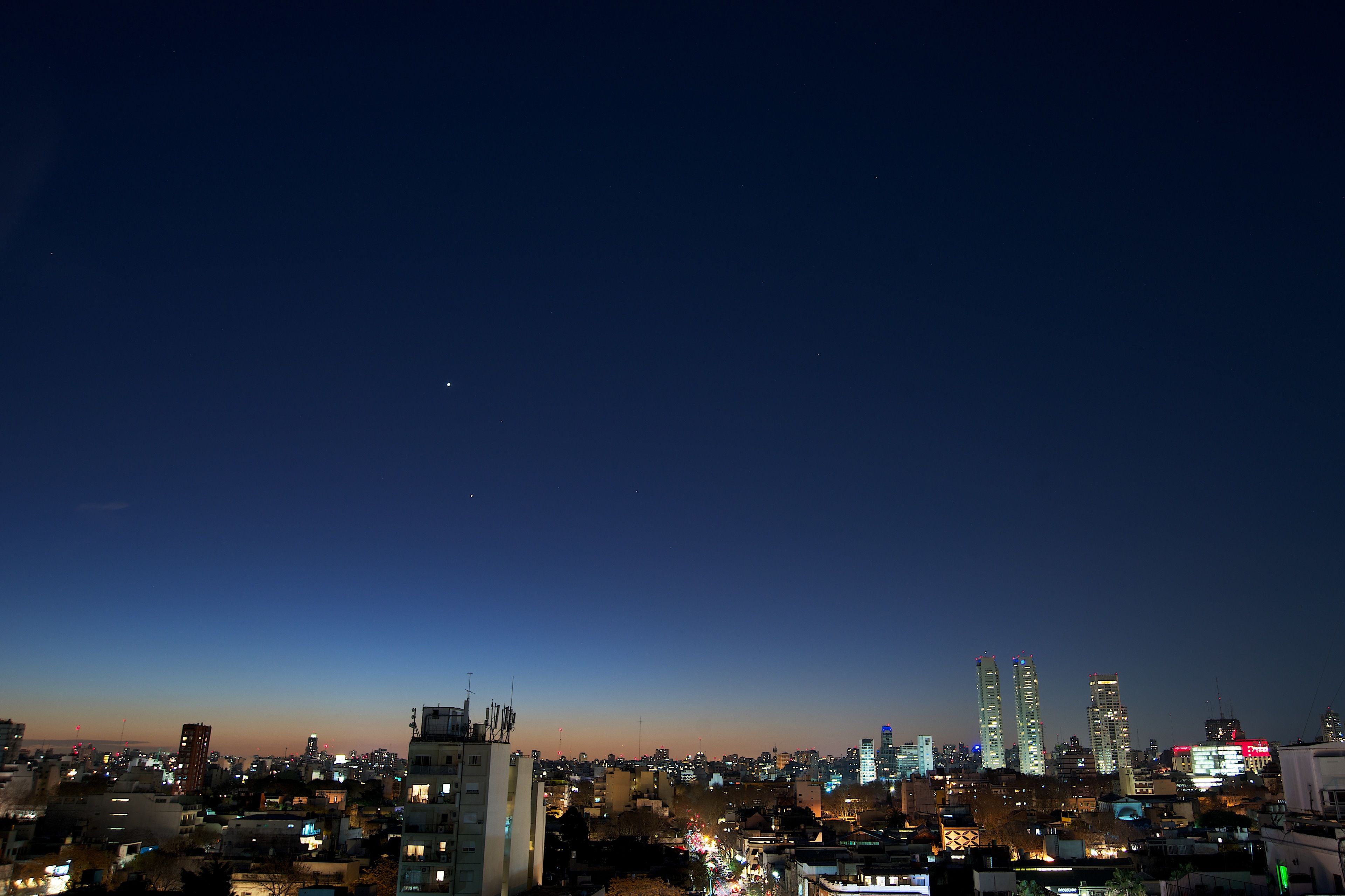 Un horizonte urbano al anochecer con edificios iluminados y cielo despejado.