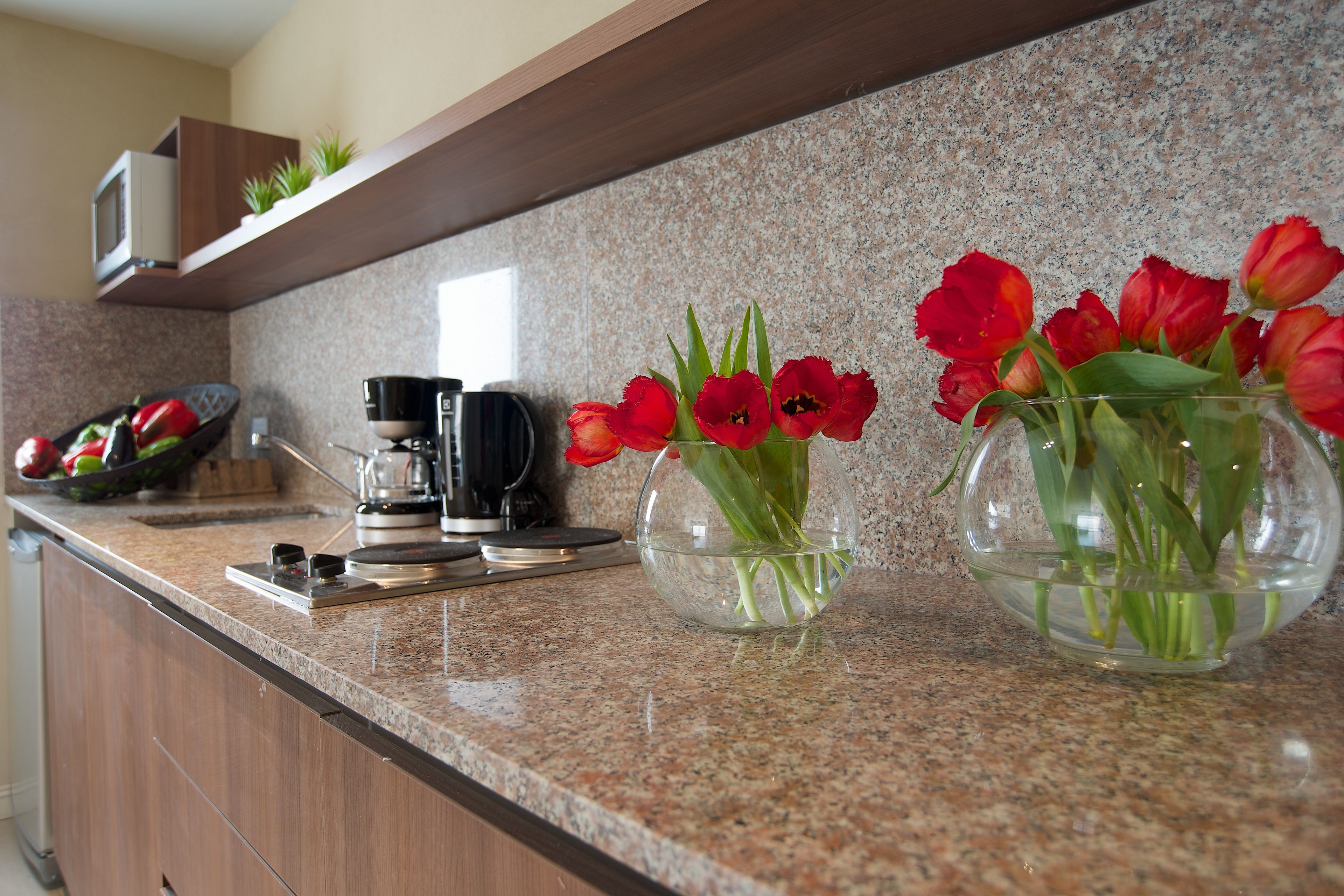 Eine Küchenarbeitsplatte mit einer Kaffeemaschine, einer Schale mit roten Tulpen und einer Mikrowelle über einem Holzboden.