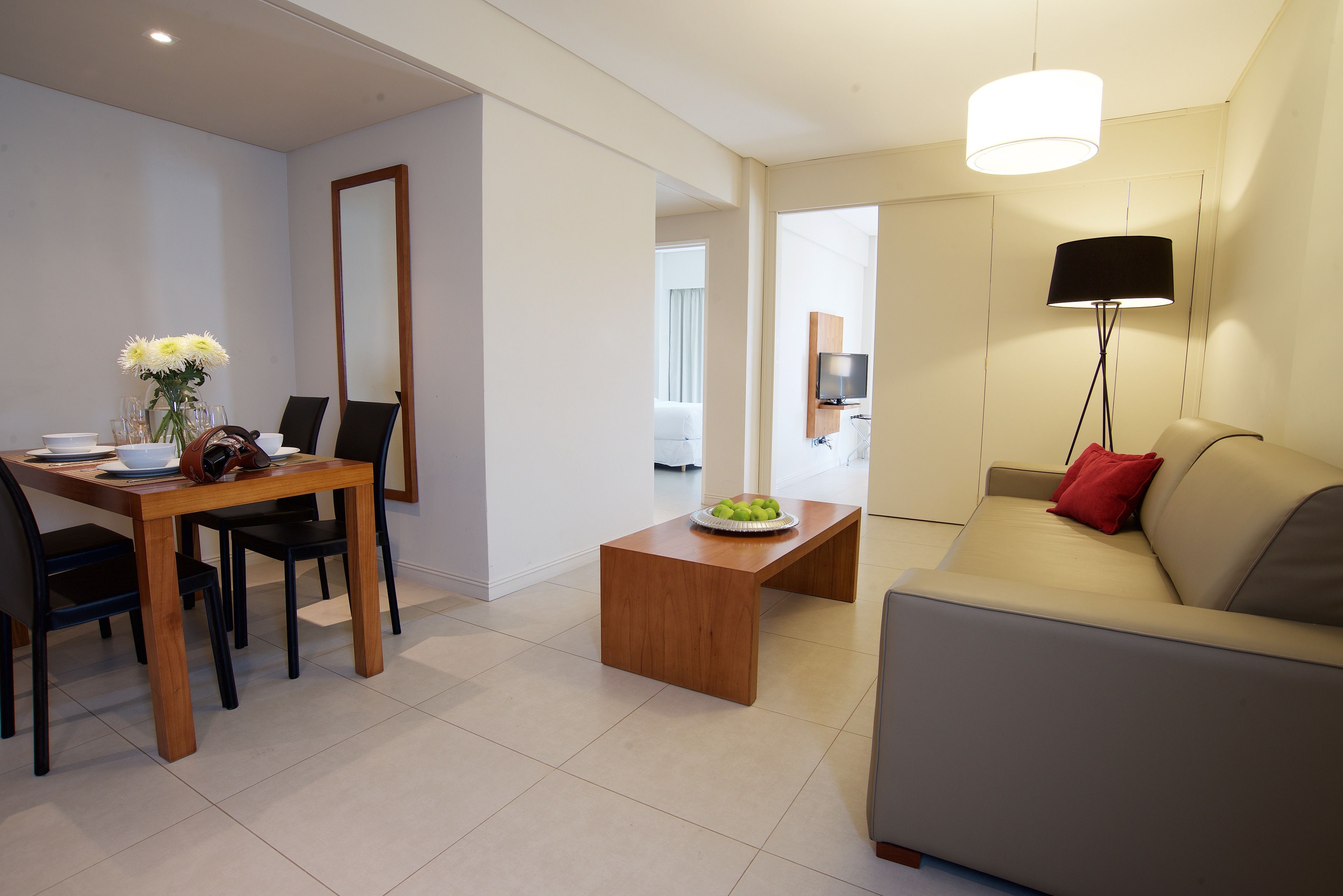 A modern living room with a sofa, a coffee table with fruit, a dining area with a table and chairs, and a TV in the background.