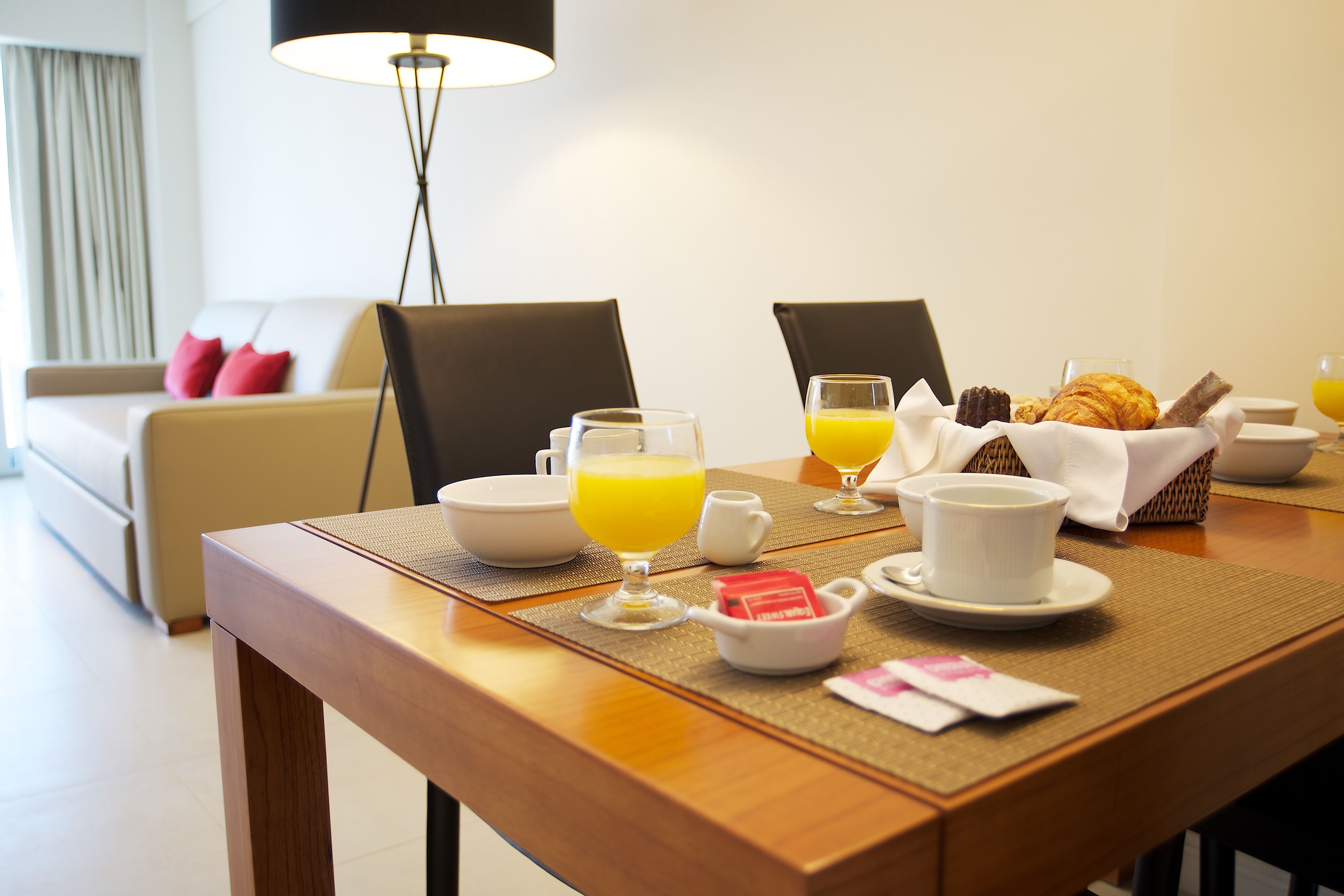 A breakfast table with croissants, orange juice, and coffee cups.