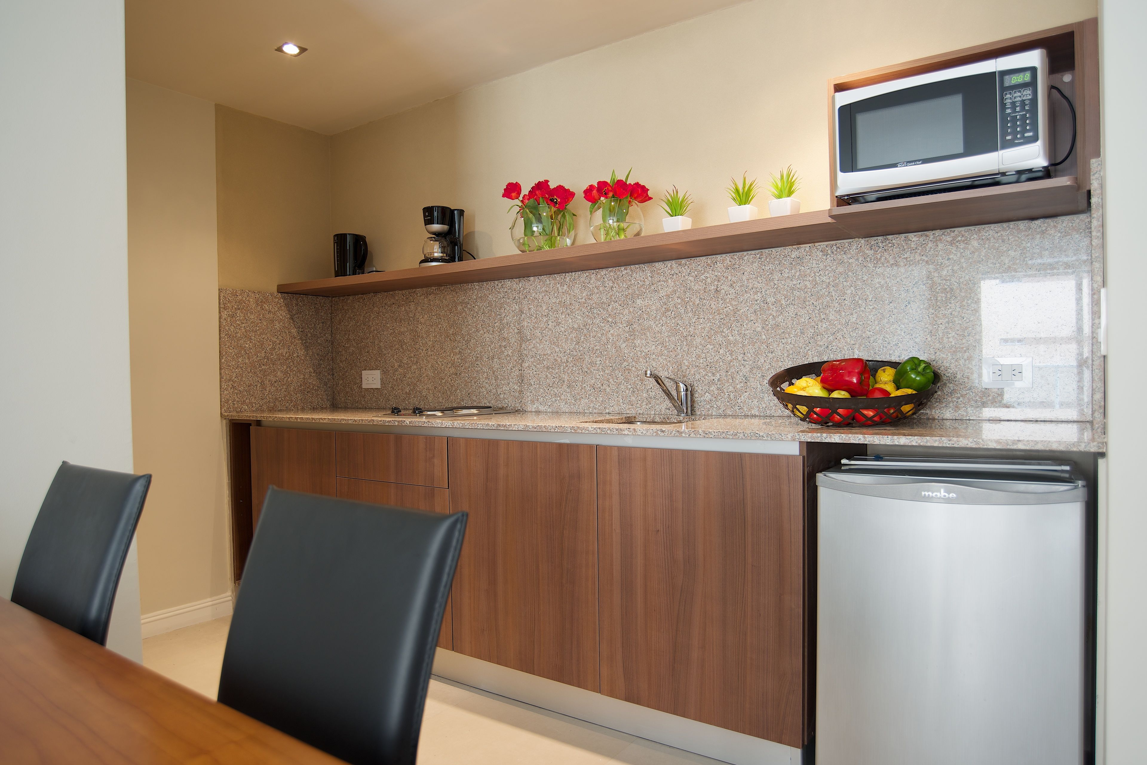 Una cucina moderna con mobili in legno, forno a microonde integrato, macchina per il caffè e una ciotola di frutta.
