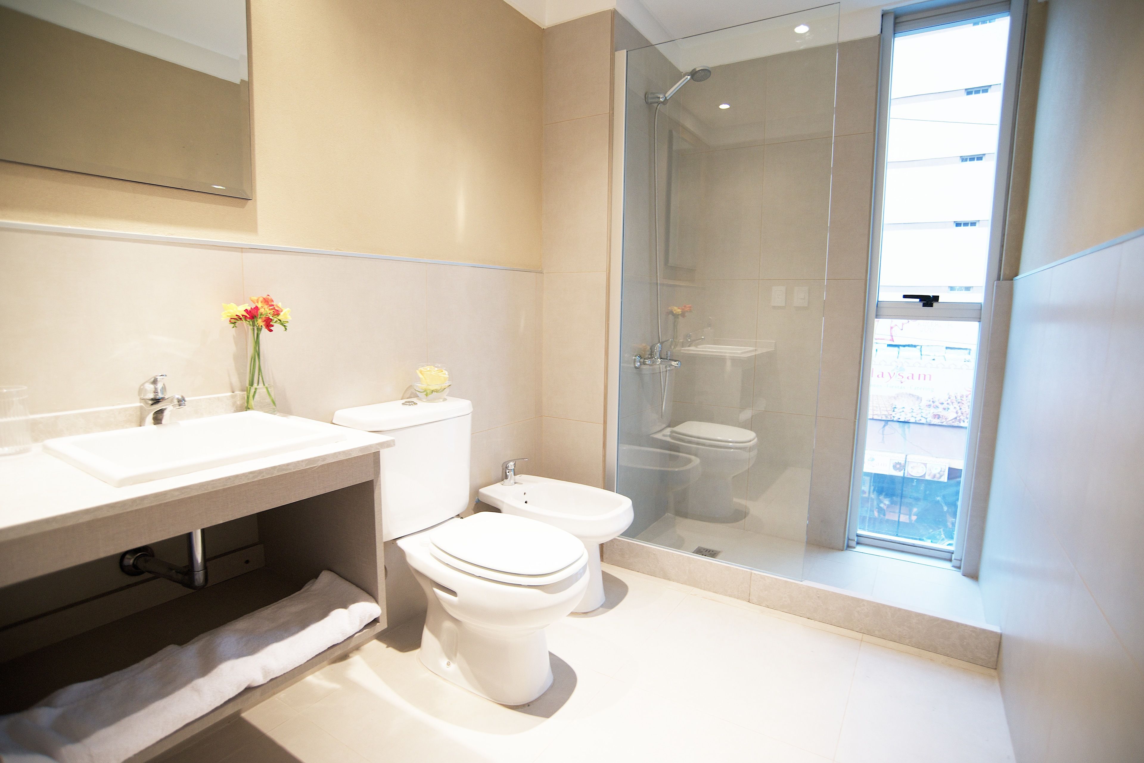 Een moderne badkamer met een douchecabine van glas, een wit wastafeltje en twee toiletten.