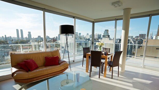 Una sala de estar moderna con una mesa de centro de vidrio, un sofá de cuero y un comedor con sillas y una mesa.