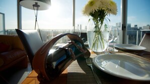 Una mesa de comedor con una botella de vino, un florero con flores y vistas a la ciudad.