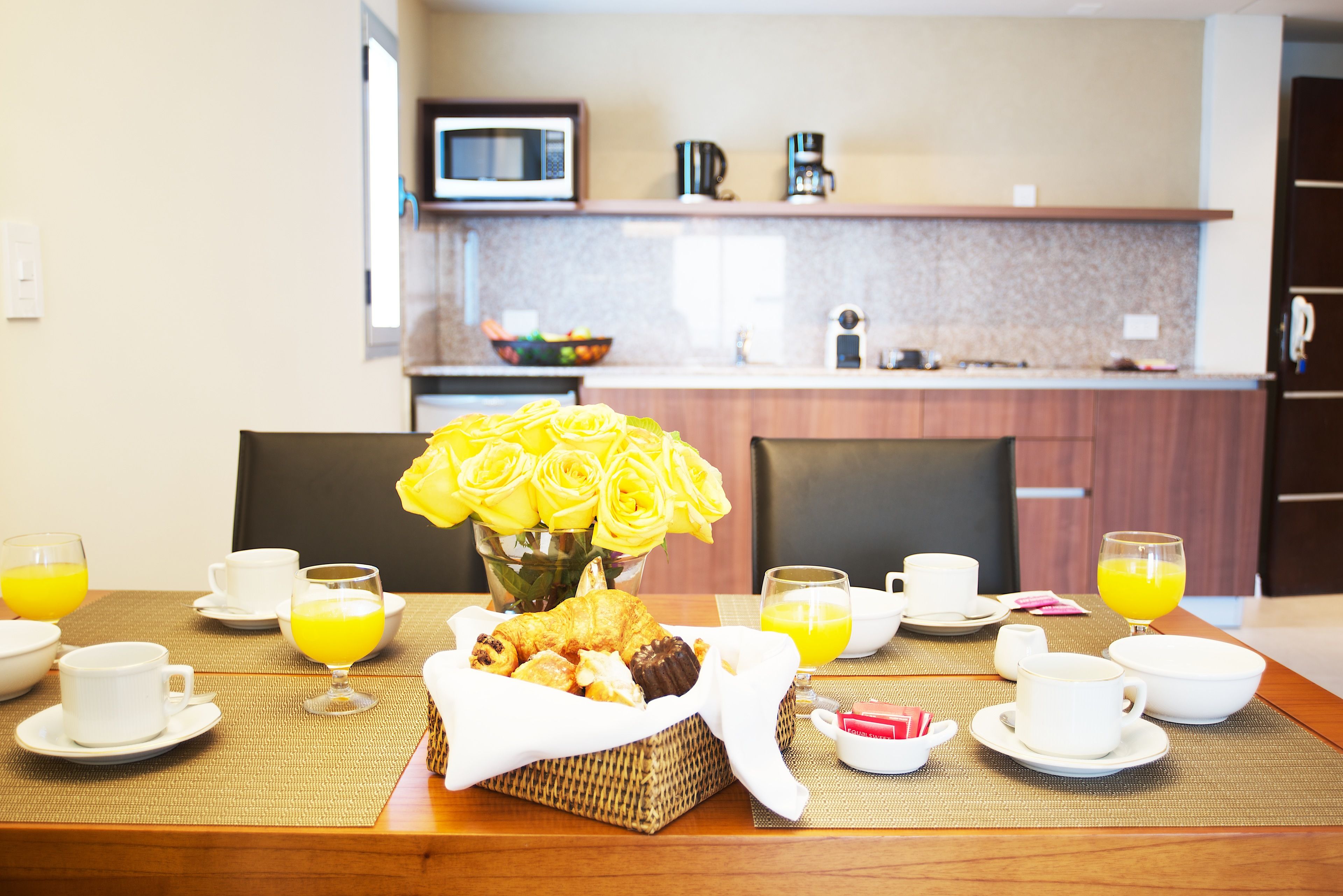 Colazione servita con tavolo per due, con croissant, cestino di pasticcini e un vaso di rose gialle.