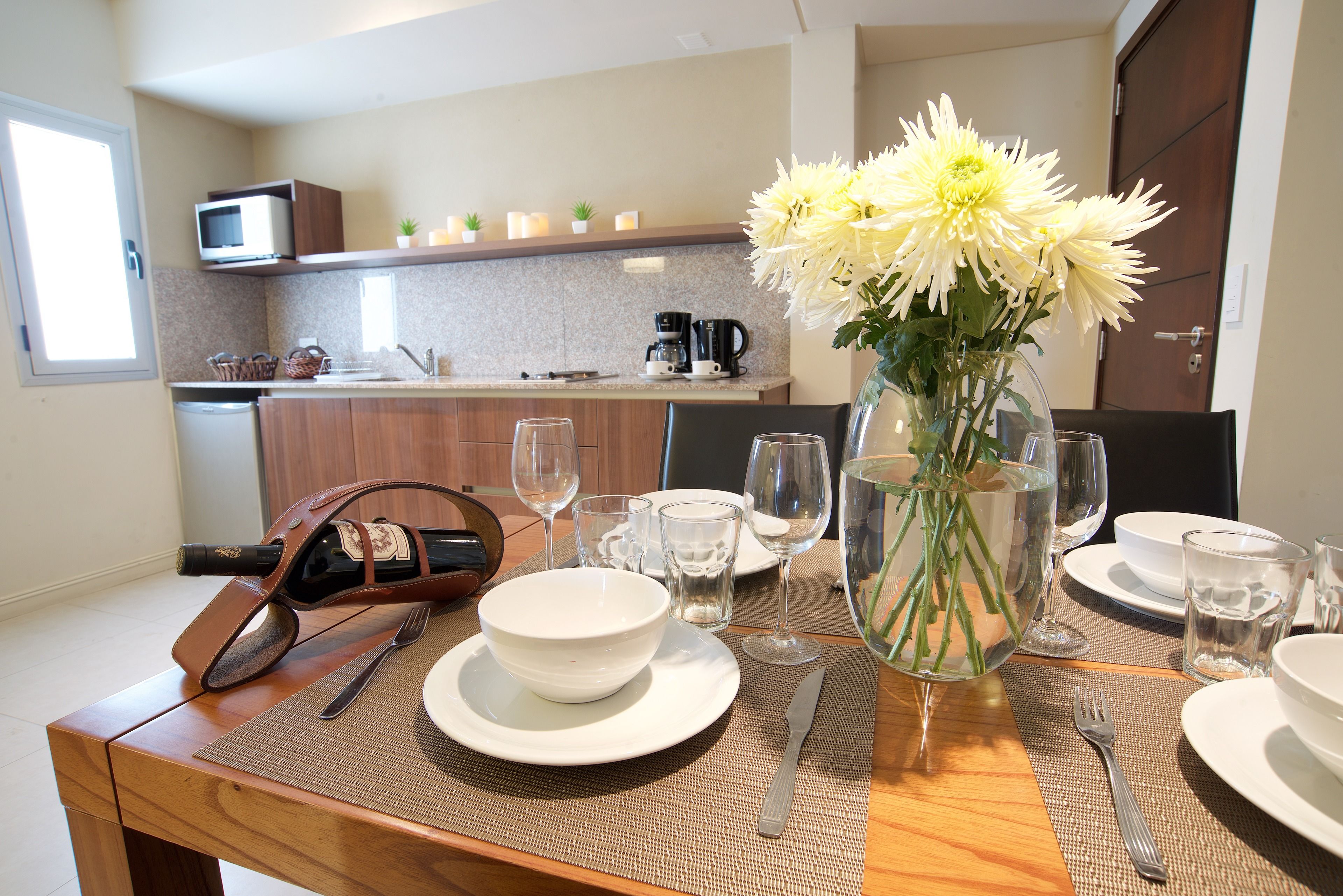 A dining table set with white plates, bowls, cutlery, and a vase with flowers.