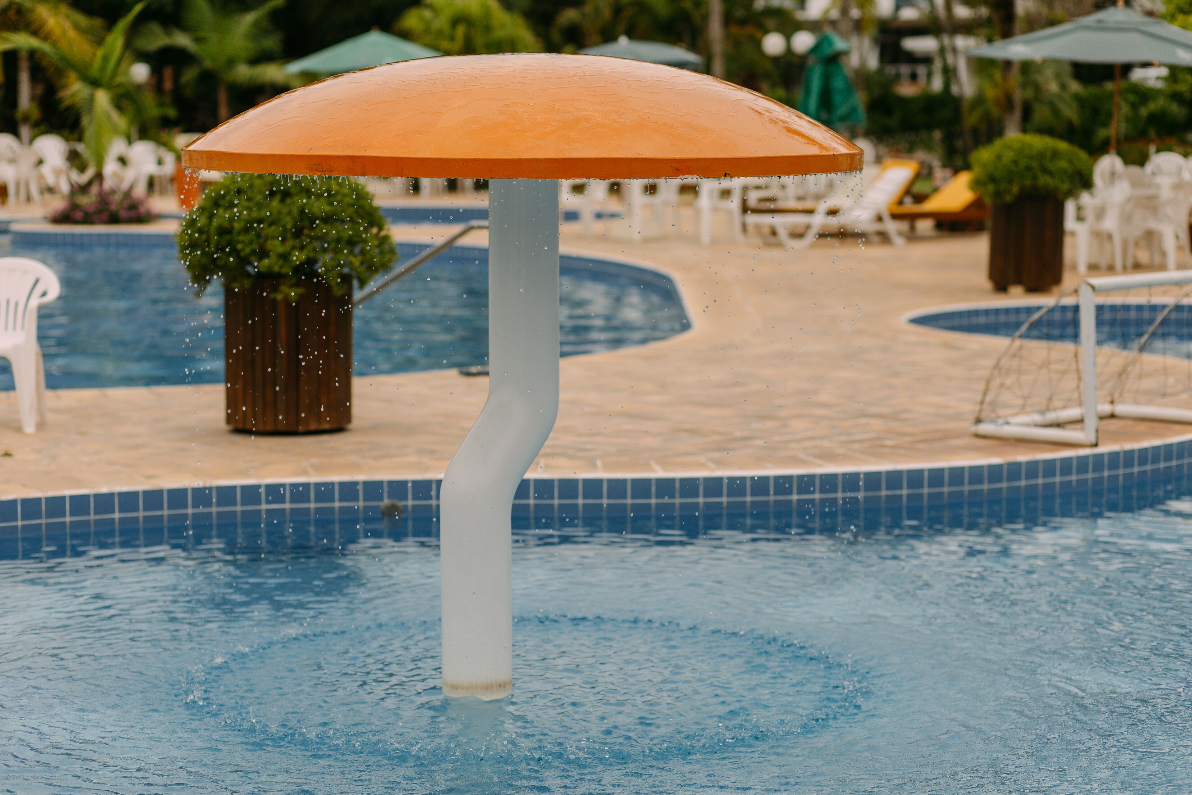 Zona de piscina con una fuente central, rodeada de sillas de descanso y sombrillas.