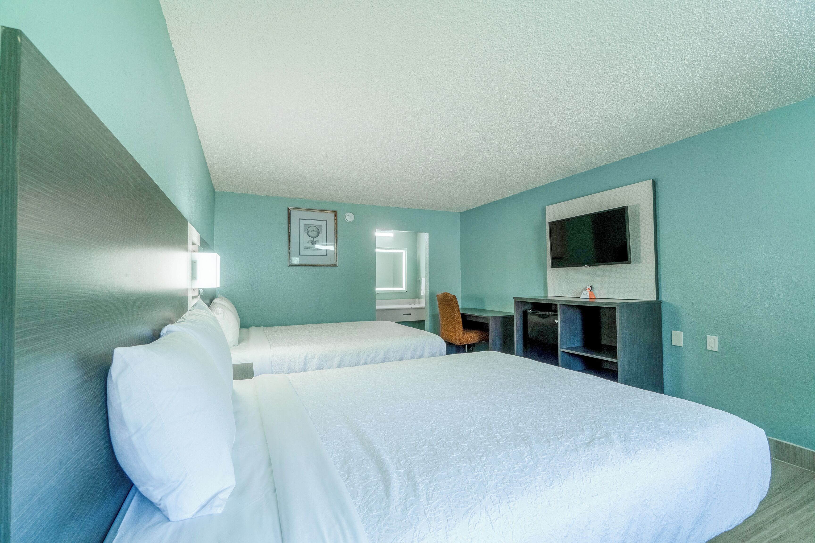 A hotel room with two beds, a desk, a chair, a TV, and a window.