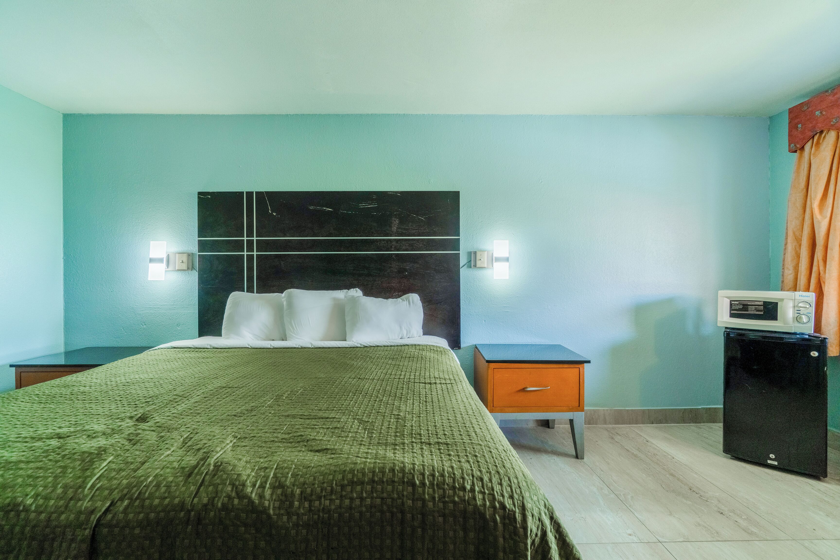 A hotel room with a bed, a nightstand, a drawer, a microwave, and a small refrigerator.