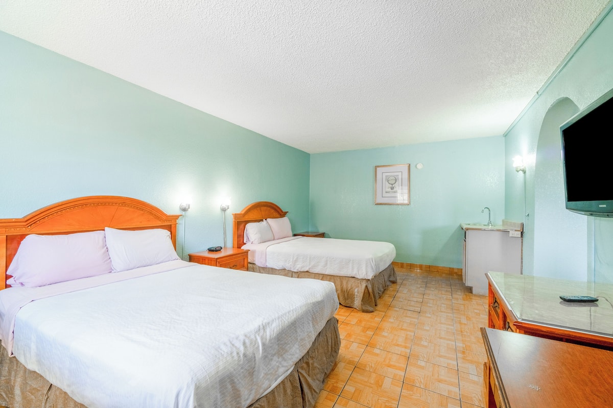 Habitación de hotel con dos camas, televisión, escritorio y una kitchenette pequeña.