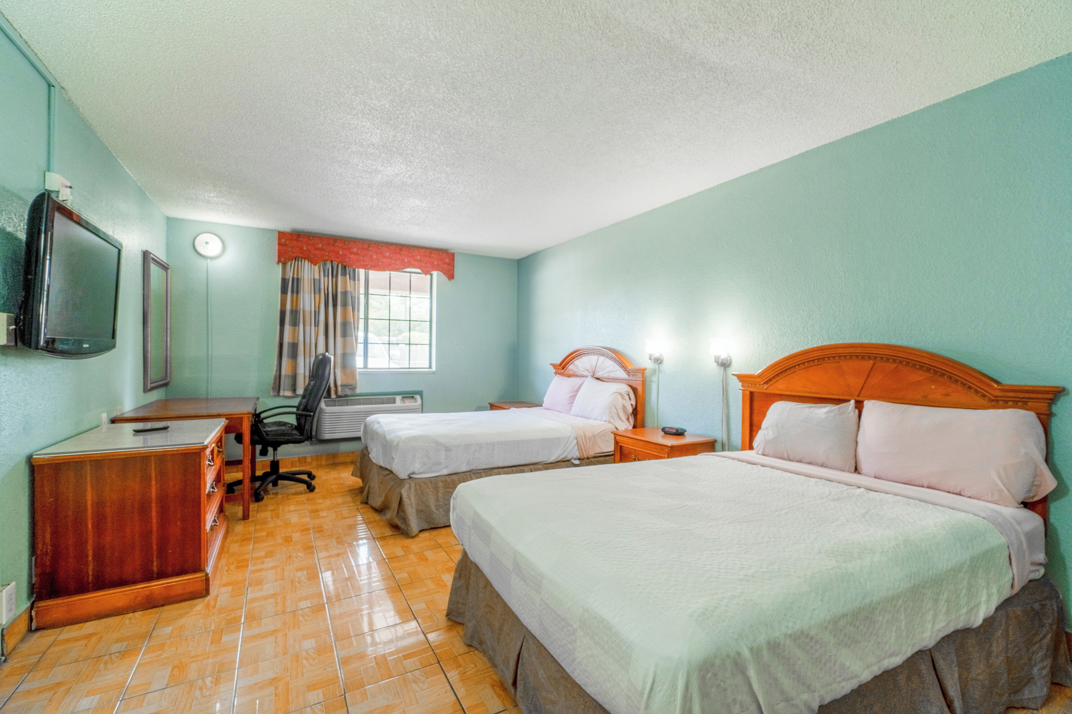 Habitación de hotel con dos camas, un escritorio, una televisión y una ventana con cortinas.