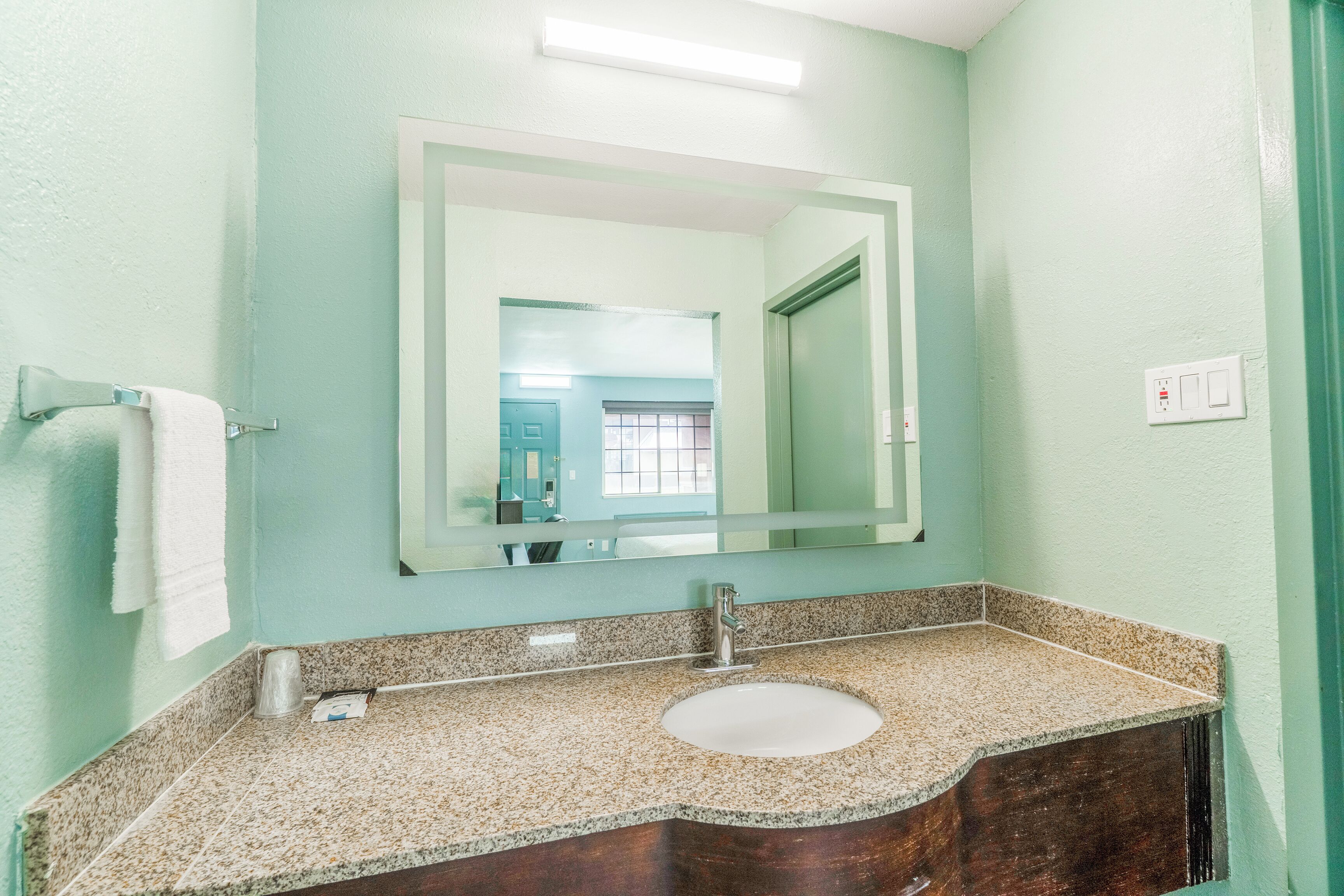 Een badkamer met een granieten aanrecht, een wastafel, een spiegel en een handdoekhouder.