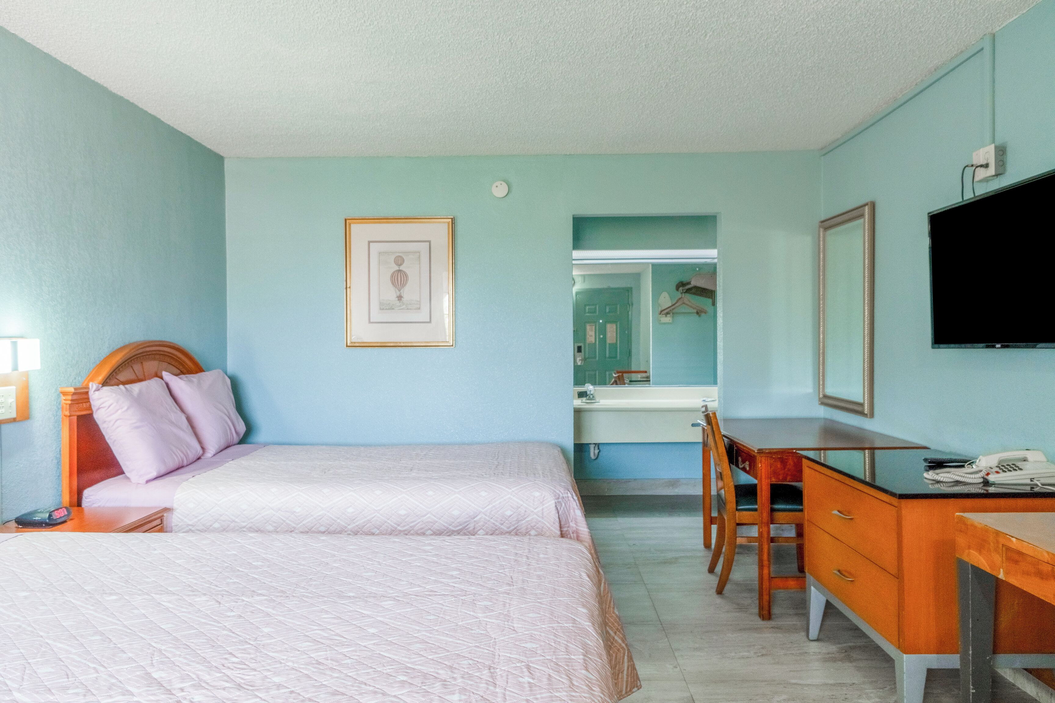 A hotel room with two beds, a desk, a chair, a television, and a bathroom visible through an open door.