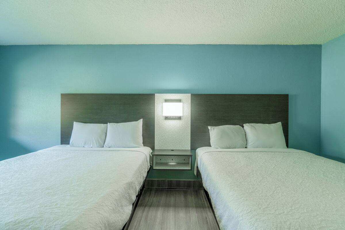 Una habitación de hotel con dos camas, una mesita de noche y una lámpara fijada a la pared.