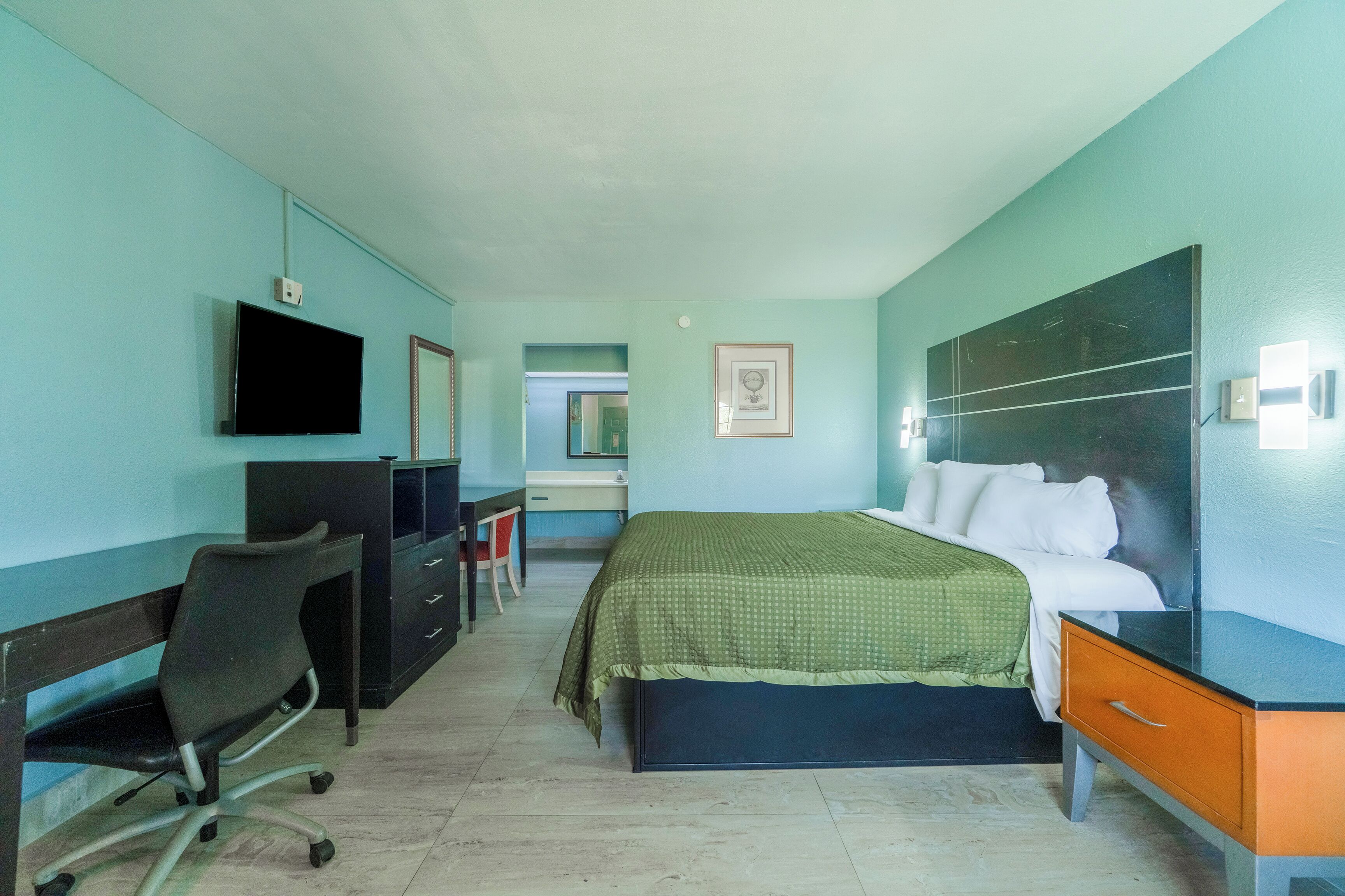 A hotel room with a bed, desk, chair, television, and a mirror.