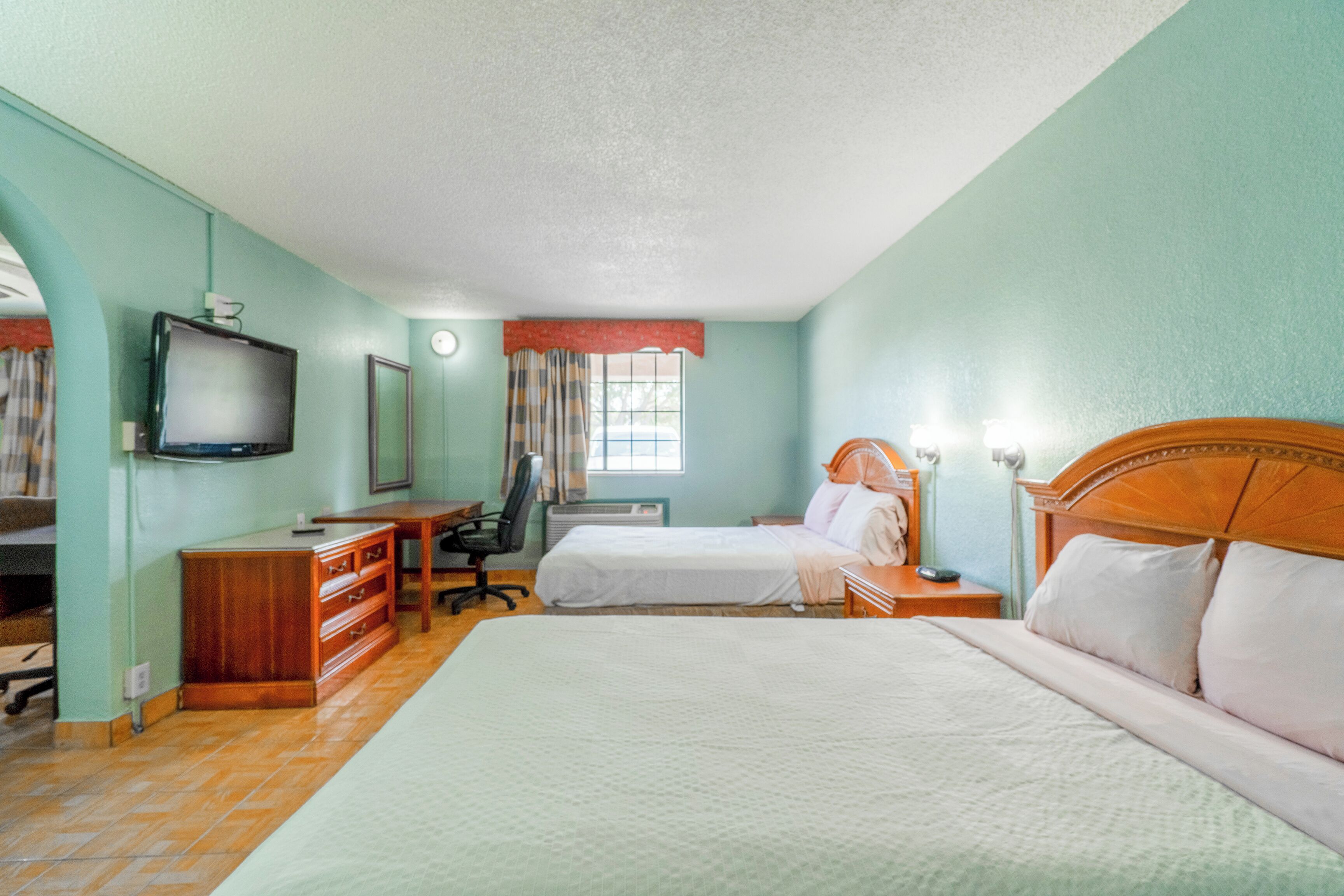 A hotel room with a large bed, a desk with a chair, a television, and a window with curtains.