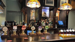 Un bar amb diverses aixetes de cervesa, una caixa registradora i una varietat de botelles i gots a les prestatgeries.