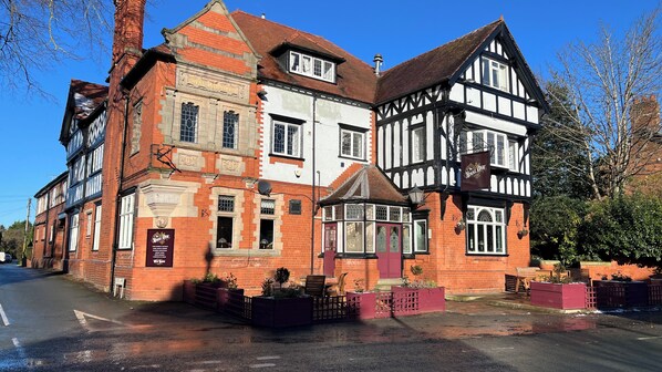 Un edificio de estilo Tudor tradicional con letrero de pub, fachada de ladrillo rojo y una tienda en la esquina.