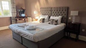 Una cama bien hecha con sábanas y toallas blancas, un cabecero acolchado y una mesita de noche con una lámpara.