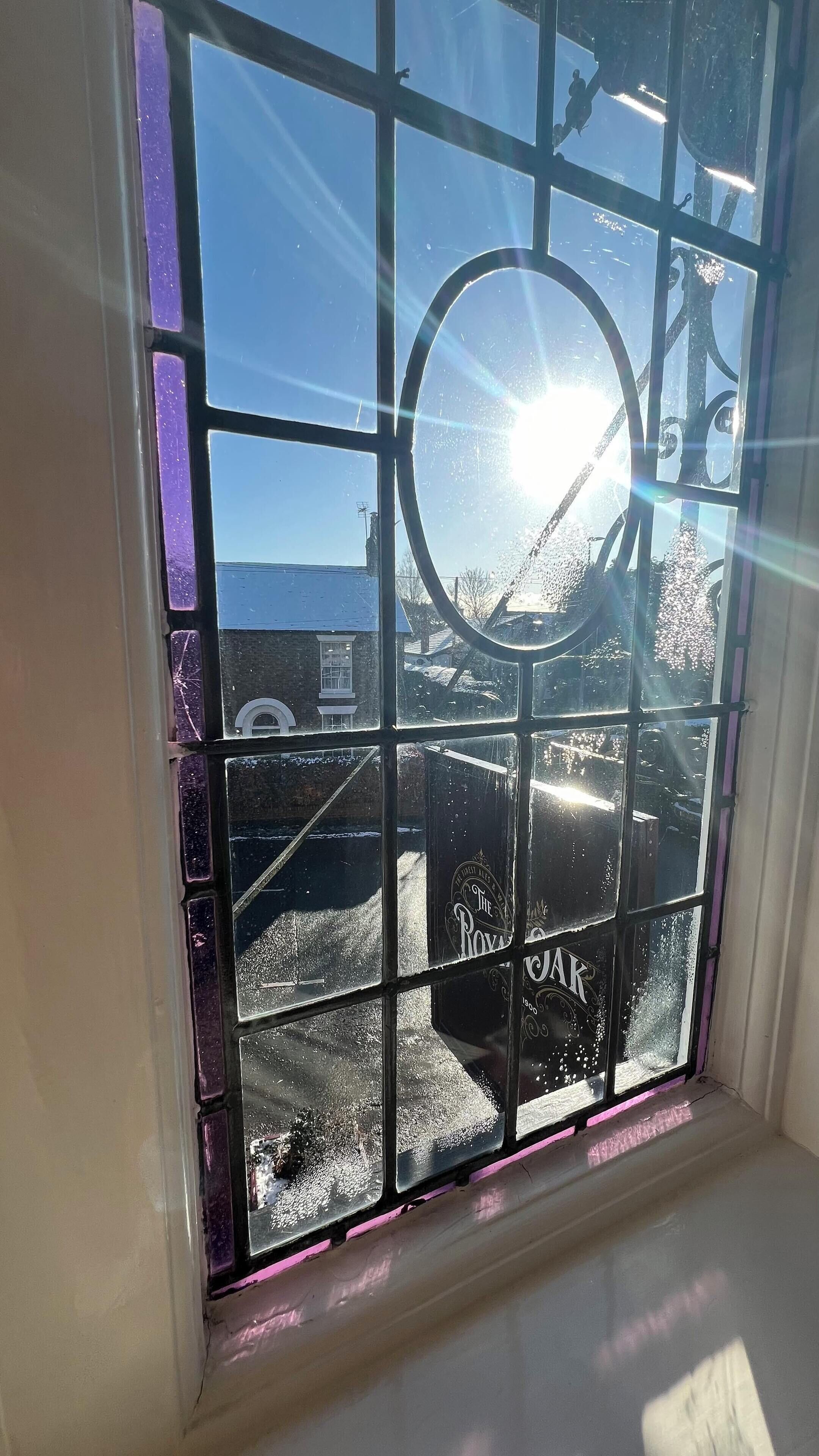 A window with a grid pattern and a circular design, featuring a view of a building and a clear sky.