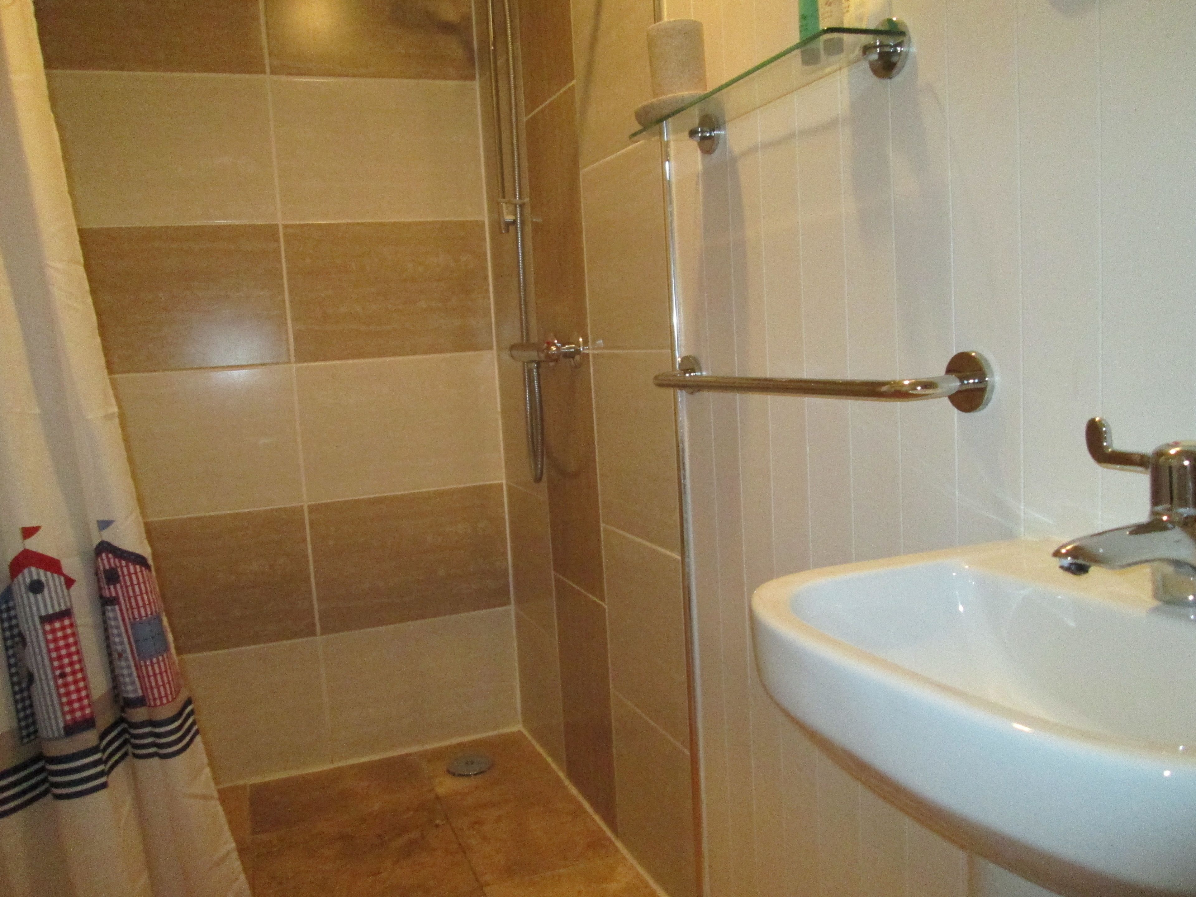 A bathroom with a glass shower enclosure, a white sink, and a towel rack with patterned towels.
