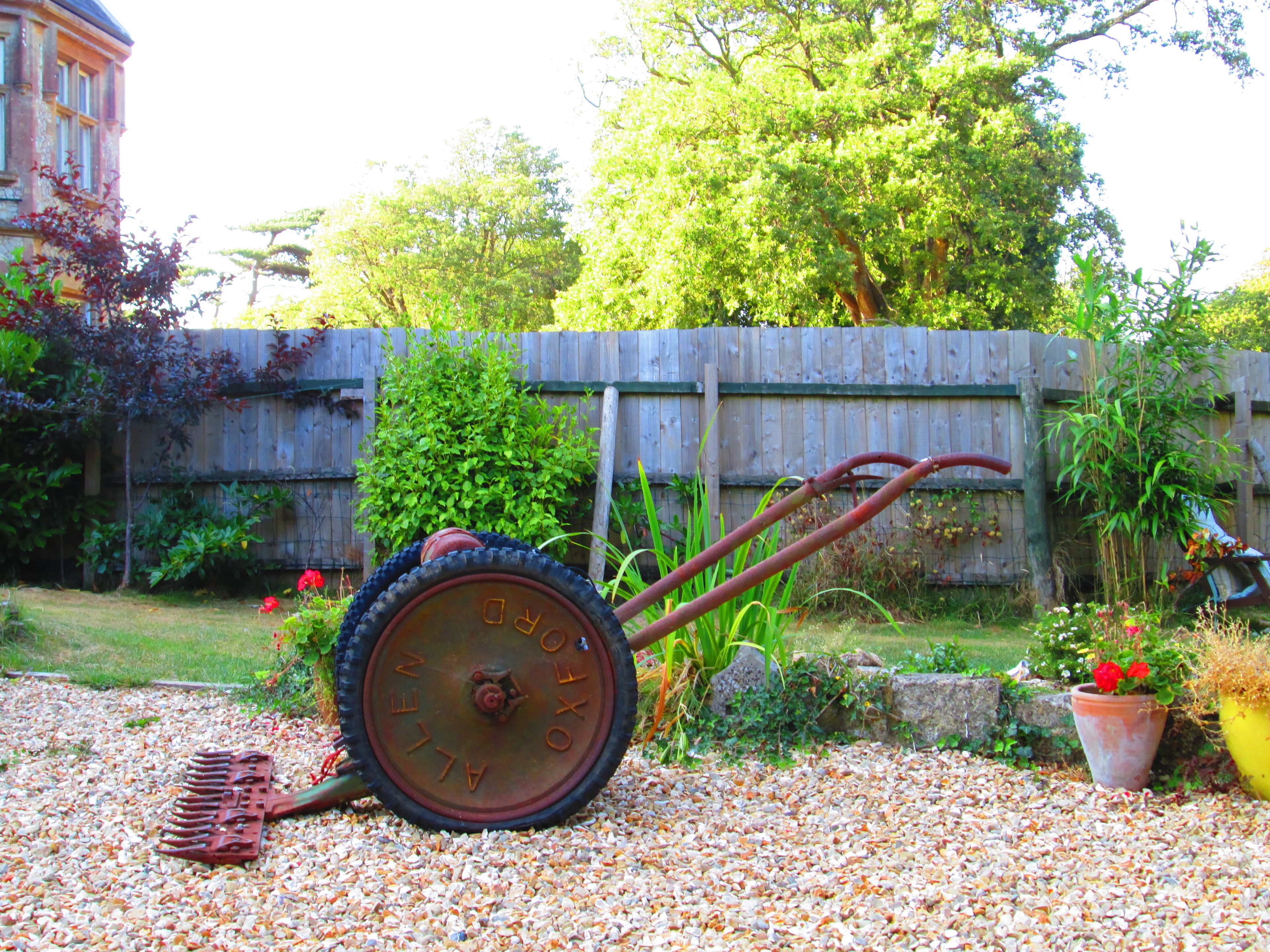 A garden with a wheelbarrow, gravel path, wooden fence, and potted plants.