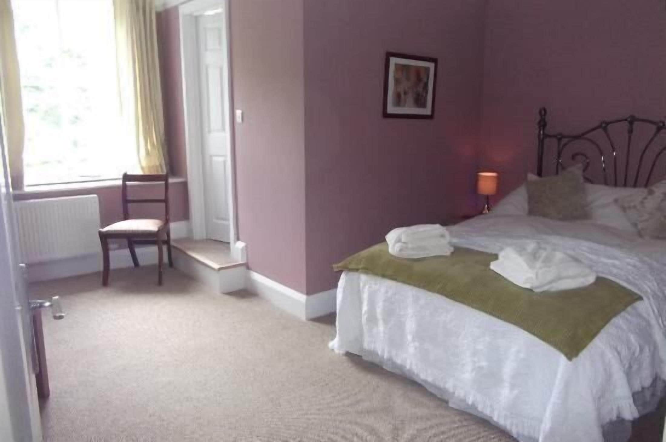 A bedroom with a bed, a chair, a picture on the wall, and a window with curtains.
