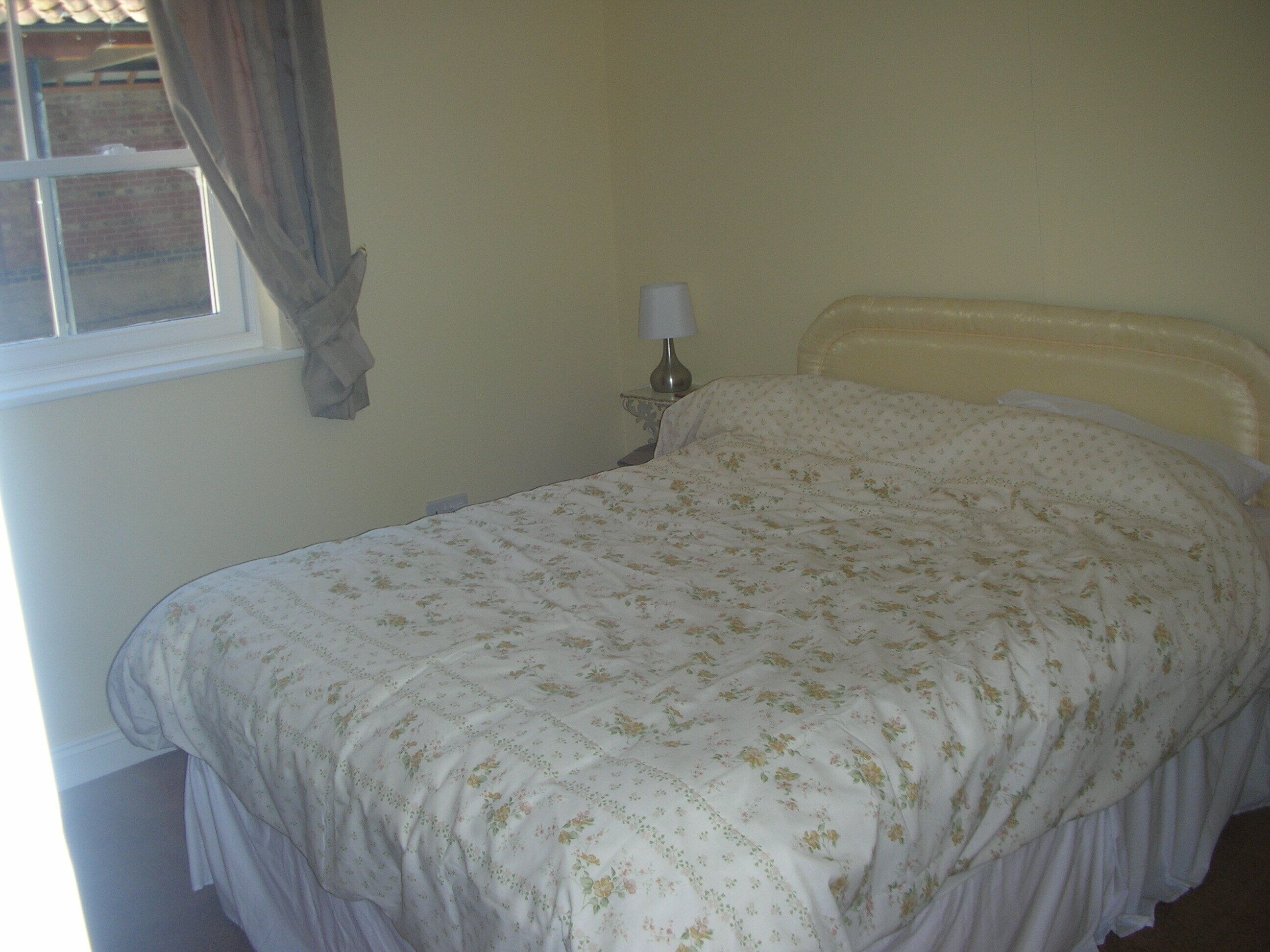 A bedroom with a bed, a nightstand, a lamp, and a window with curtains.