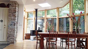 Ein großzügiger Essbereich mit einem großen Holztisch und Stühlen, einer Wand aus Steinziersteinen und Blick auf Grün durch große Fenster.
