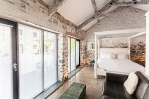 A bedroom with a stone wall, a white canopy bed, and large windows with blinds. - Anrán at Tidwell Farm (Newton Abbot)
