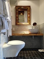 A bathroom with a white toilet, a wooden vanity with a white sink, and a mirror with a floral frame.