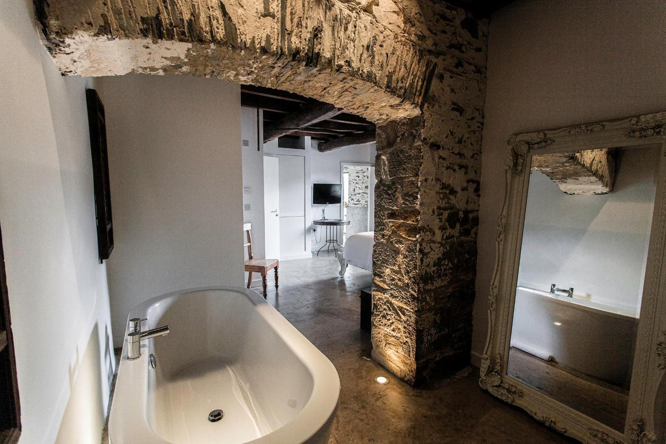 A bathroom with a freestanding bathtub, a stone wall, and a mirror with a decorative frame.