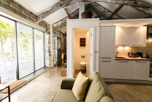 Un interior moderno con un sofá, una cocina con armarios blancos y un ventanal con persianas.