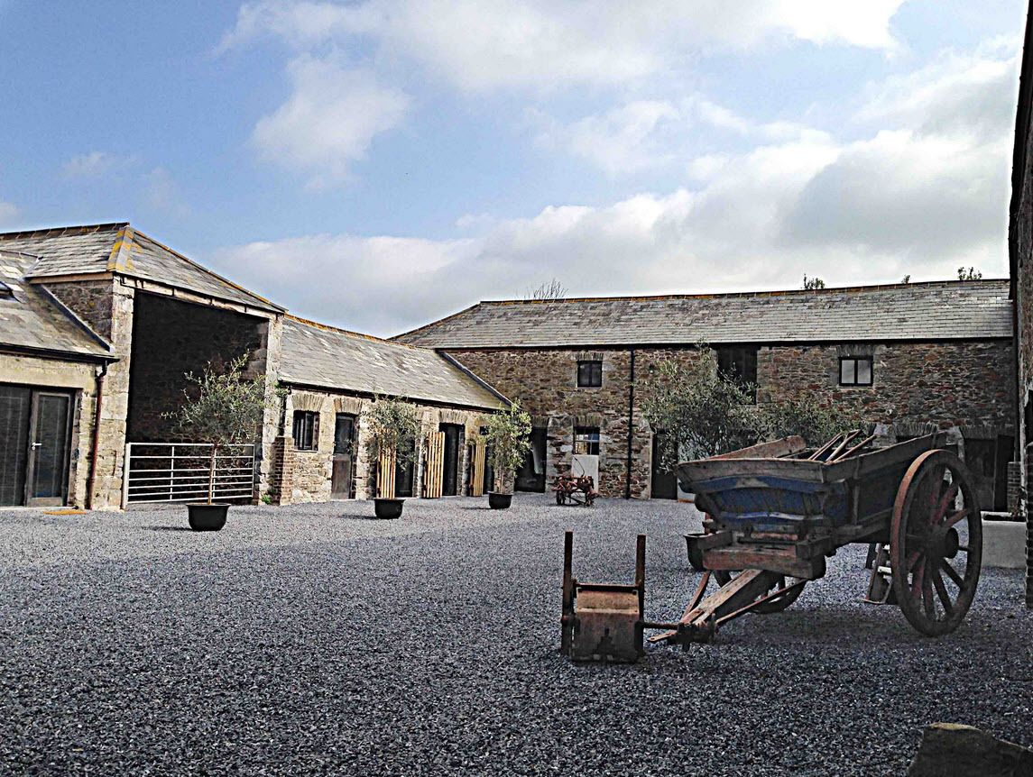 A rustic building with a gravel courtyard, a wooden cart, and a stone wall.