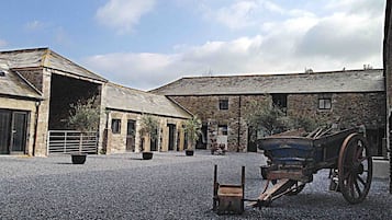 A rustic building with a gravel courtyard, a wooden cart, and a stone wall.
