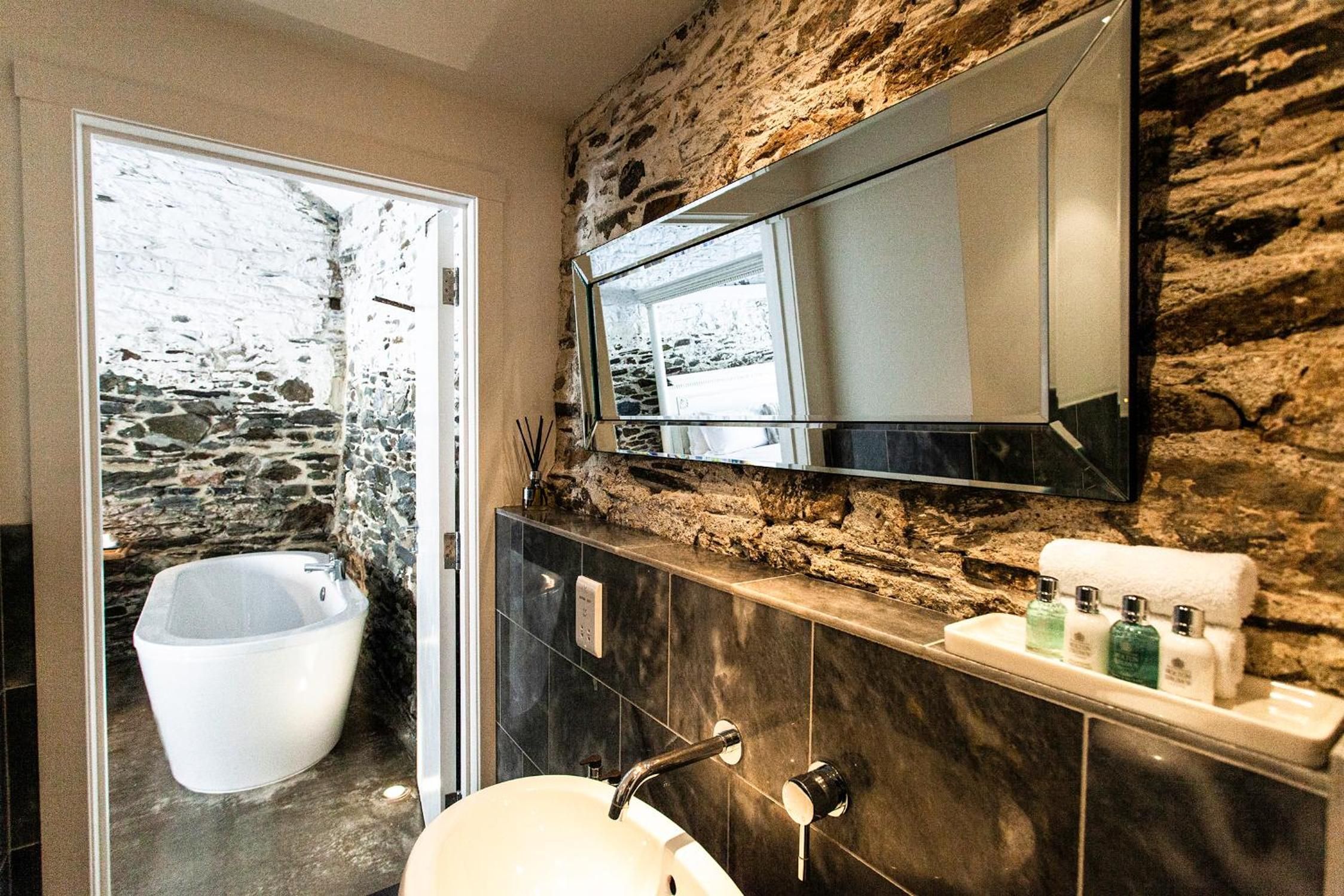 Une salle de bain avec un mur en pierre, une baignoire, un lavabo et un miroir.