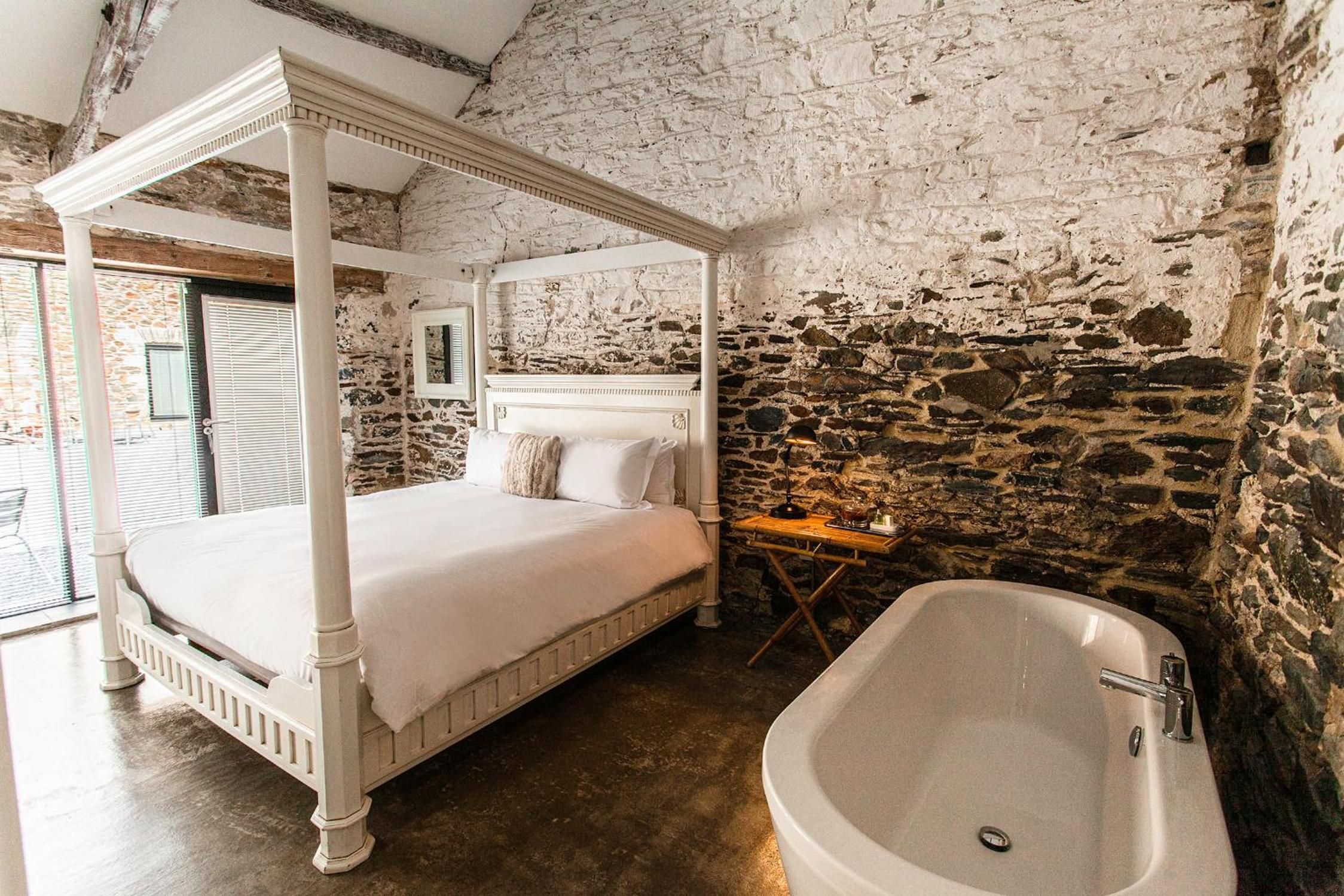 A four-poster bed with a headboard, a stone wall, and a freestanding bathtub.